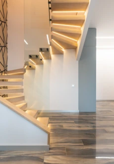 Modern interior featuring dark, wood-look plank flooring on the main level transitioning to solid wood treads on a floating staircase with a contemporary glass railing.