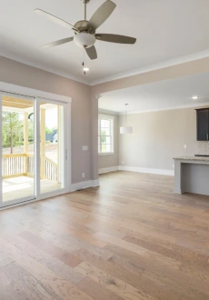 Empty, open-concept living room with medium-width, natural-finish oak hardwood flooring, beige walls, white trim, and a sliding glass door leading to a screened-in porch.