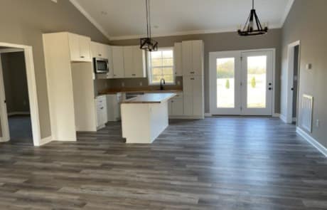 Open-concept kitchen and living area featuring wide plank gray luxury vinyl plank (LVP) flooring Nashville with white cabinetry, a kitchen island, and a door leading to the outside.