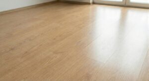 A wide shot of a sparkling clean, shiny light brown laminate floor reflecting sunlight from a nearby window, showcasing the successful 'after' cleaning result.