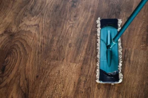 A mop with a teal handle and blue head rests on a wooden floor with a clear, natural wood grain.