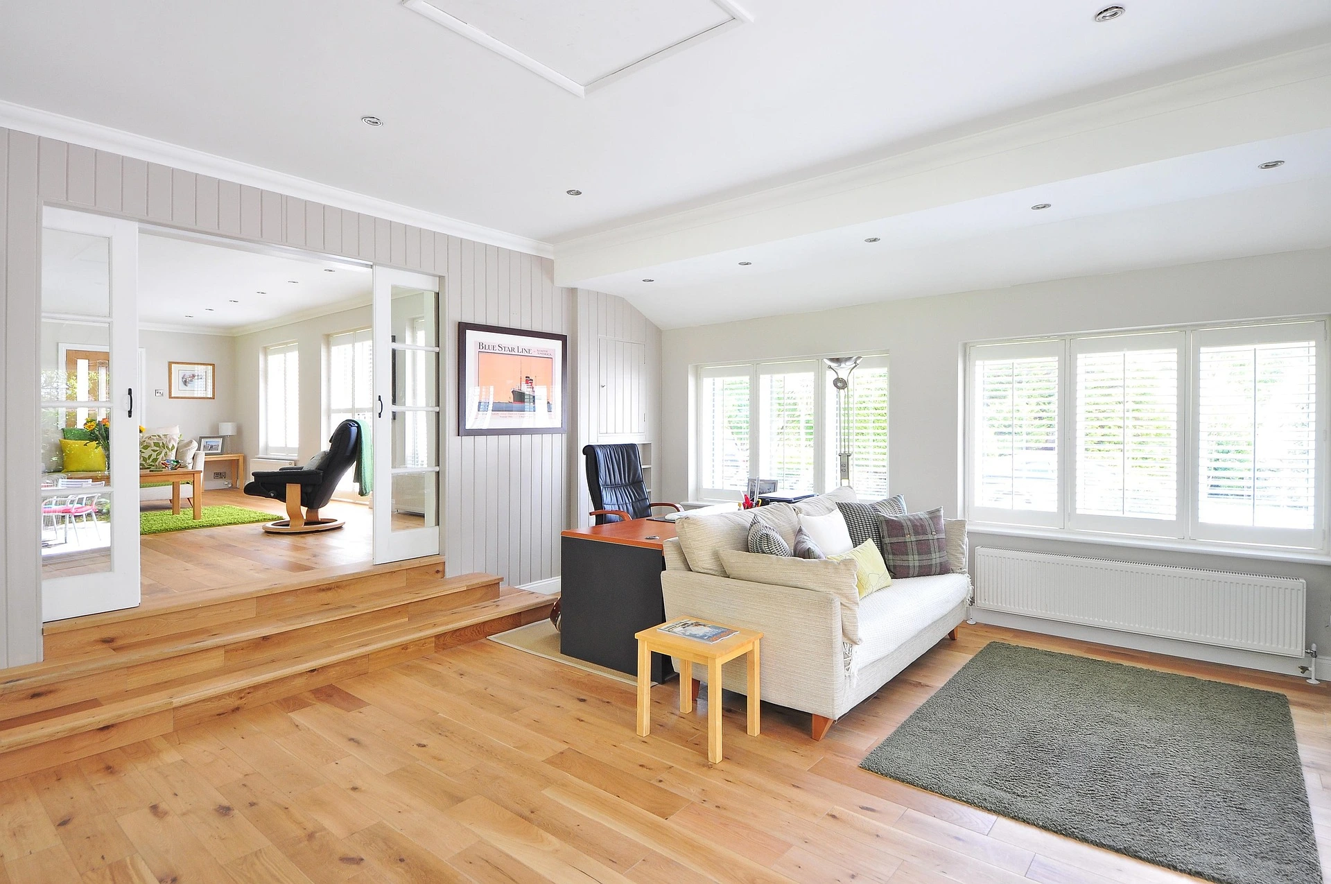 A bright and modern living room with light wooden floors, white walls, and comfortable seating.