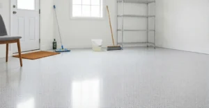 A bright, clean room with a white flecked epoxy floor, featuring a doormat, soft broom, microfiber mop, and cleaning bucket.