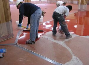 A professional flooring installer wearing black spiked shoes walks across a wet, brilliant white epoxy surface. The installer is using a roller to ensure a smooth, even application, while the specialized footwear prevents footprints in the fresh coating.
Types-Of-Epoxy-Floor-Coatings