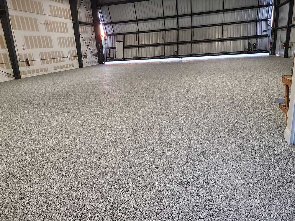 A clean, spacious residential garage featuring a polished epoxy floor. The base is a sleek grey, heavily speckled with blue, silver, and white decorative flakes, creating a textured, granite-like appearance with a mirror-like reflective finish.